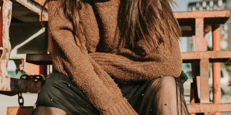 woman in brown sweater sitting on brown wooden bench during daytime