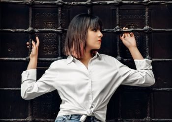 woman in white dress shirt leaning and holding on metal mesh wall