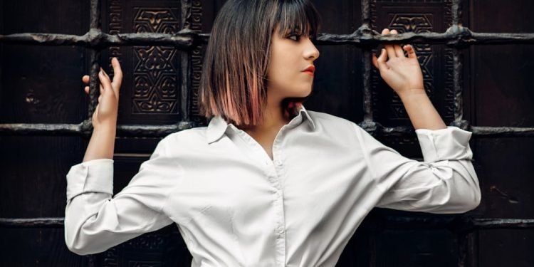 woman in white dress shirt leaning and holding on metal mesh wall