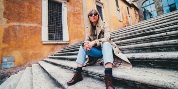 woman in brown coat and blue denim jeans sitting on stairs