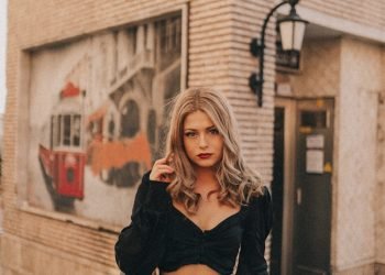 woman in black cardigan and white crop top standing near brown brick building during daytime