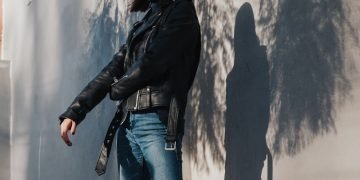 woman in black leather jacket and blue denim jeans standing beside white wall