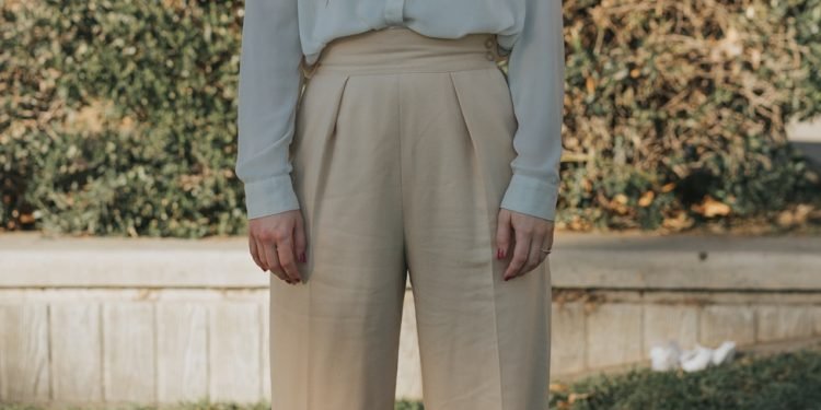 woman wearing gray button-up long-sleeved shirt and brown pants standing in front of bushes