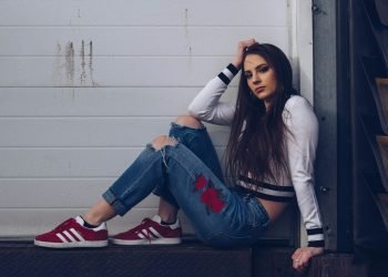 woman in white long sleeve shirt and blue denim jeans sitting on white wooden fence