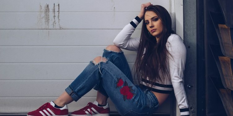 woman in white long sleeve shirt and blue denim jeans sitting on white wooden fence